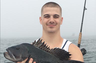 A man holds up the sea bass he caught.