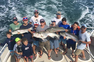 View from atop the boat looking down at the deck at a group of 13 men and boys holding up the striped bass they caught.