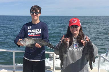A young man and woman each hold up the 3 sea bass they caught.