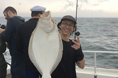 A man smiles as he holds up a large fluke.