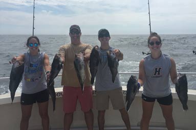 A father and his three adult triplets, 2 young women and a man, each hold out 2 sea bass and smile for the camera.