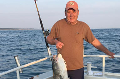 A man holding up the striped bass he caught with a hook.