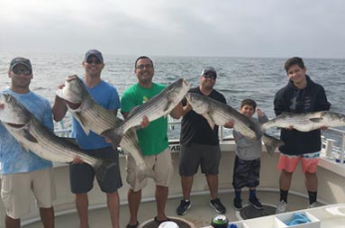 Six men and a young boy all smile and each hold up striped bass./><span class=