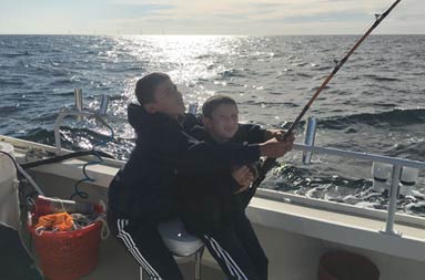An adolescent boy helps his younger brother hold onto the reel and pull in his catch.