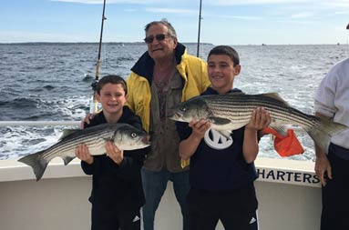 A grandfather stands between his two grandsons, each holding up a striped bass.