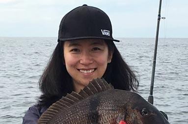 Closeup of a woman wearing a black baseball cap holding up the large porgy that she caught.