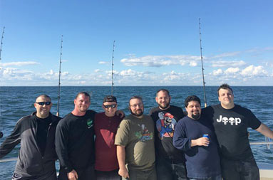 Seven men stand at the back of the boat with the reels behind them smiling for the camera.