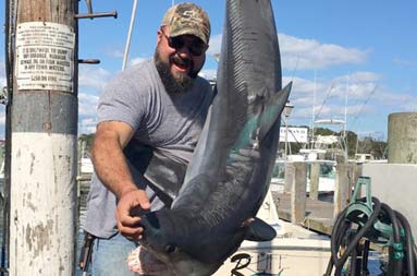 A man stands next to and poses with the shark he caught.