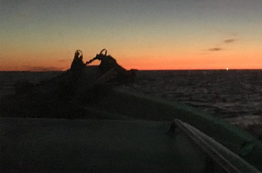 Looking out from inside the boat at the dark water and orange/yellowish sky with the sun rising far in the distance.