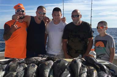 Three men, a teenage boy and younger boy stand behind the fillet table with a pile of whole sea bass laid out ready to fillet.