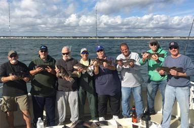 Eight men each hold up 1 blackfish (tautog).