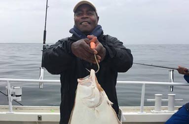 A man wearing a baseball cap and sunglasses holds up the large fluke he caught.