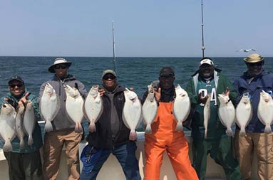 A group of six men standing on the boat each holding up two fluke.