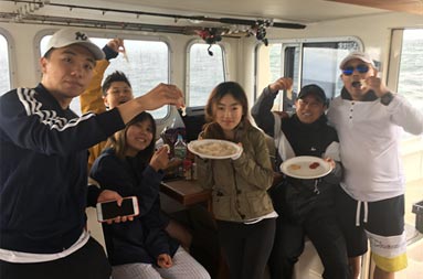 A group of six people stand inside the cockpit holding up their pieces of fluke sashimi.