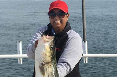 A woman smiles while holding up a striped bass.
