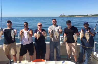 On a sunny day with the lighthouse behind them in the distance, five men and one woman smile as each hold up 2 scup.