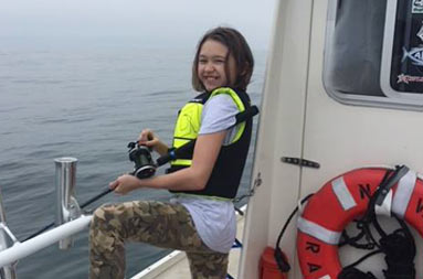 An adolescent girl smiles for the camera while she holds onto the reel waiting for a bite.