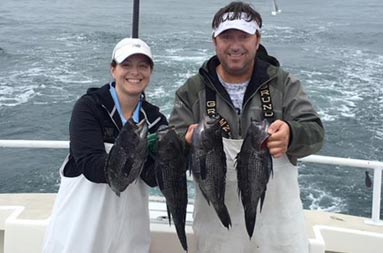 A woman and man smile for the camera as they each hold up 2 scup.