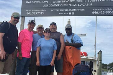 Four men and one woman stand next to first Mate Gil, who gives a thumbs up in front of the November Rain sign at the dock.