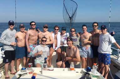 A group of 12 guys smile for the camera aboard the boat on a sunny day on the water.