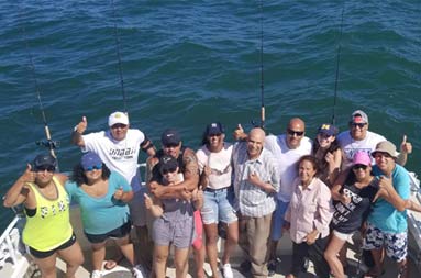 A large family of 13 look up at the camera from the deck and gives thumbs up.