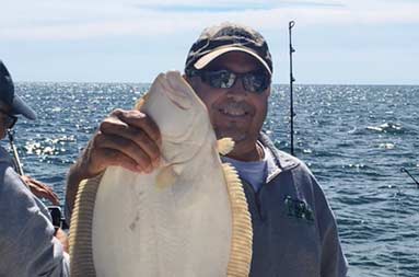 A man smiles for the camera, holding up a fluke with one hand.