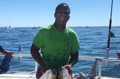 A teenage boy smiles for the camera as he holds up 2 striped bass, one in each hand.