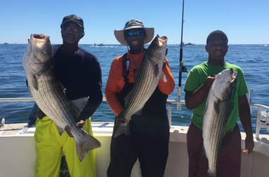 Two men and a teenage boy each smile for the camera and hold up a striped bass.