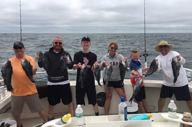 A group of 3 adults and three children hold up the sea bass they caught.