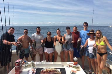 A group of men and women gathered around the boat smiling for the camera as they hold up some of the fish they caught.