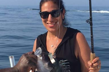 A woman smiles and holds up the fish she caught.