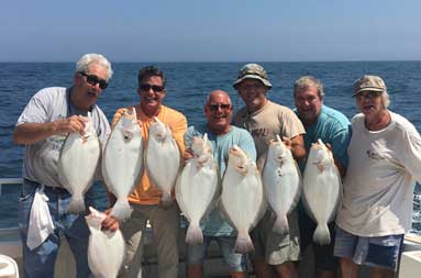Six men smile and hold up 2 fluke each.