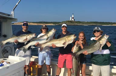 A group of 4 men and a woman each hold up striped bass.