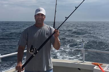 With the water behind him, A man holds up a rod for the camera.