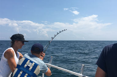 On a sunny blue-sky day, two people hold onto the rod trying to reel in their catch.