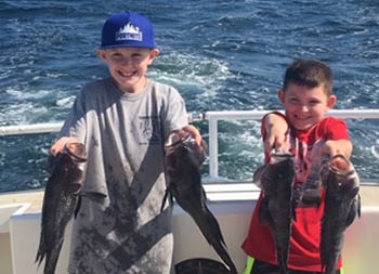Two young boys each smile and hold up 2 sea bass.