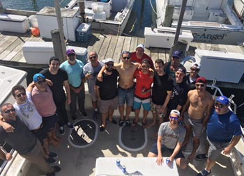 Back at the dock, a view from atop the boat looking down at the deck at a group of 17 men smiling for the camera.
