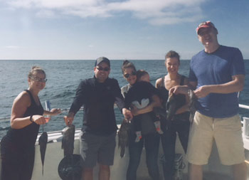 Two women and two men hold up sea bass, while a third woman holds her baby son.