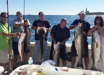 Five men and one woman standing at the far right each hold up striped bass.