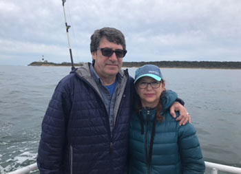 On an overcast fall afternoon, a father and daughter stand together and smile for the camera with the Montauk lighthouse in the background.