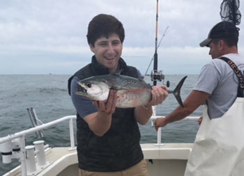 A young man proudly holds up the false albacore he caught.