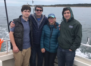 A father, his daughter and two sons smile for the camera with the lighthouse behind them in the distance.