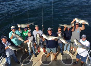 View from atop the boat looking down at the deck at a group of 10 men ranging in age, holding up their striped bass for the camera.