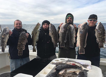 On a cold fall day on the water, a group of 4 men hold up the fish they caught.