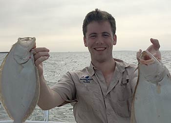 A young man holds up two fluke, one in each hand.