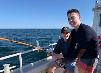 Two young men smile for the camera while holding onto the reel and waiting for a bite