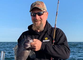 Another man with a beard, baseball cap and sunglasses holds up a sea bass.