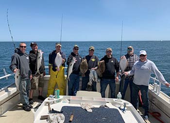 A group of 8 men each hold up the fish they caught.