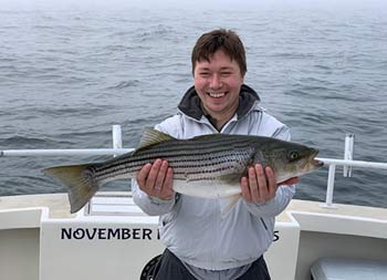 A man smiles and holds up the striped bass he caught.