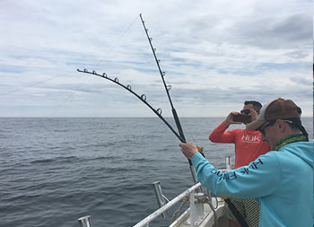 A man takes a photo of another man with his reel in the water waiting for a bite.